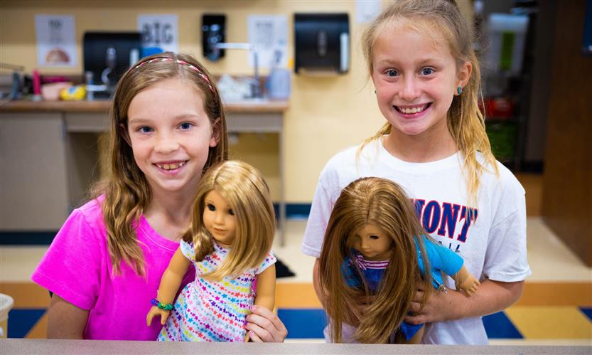 Two girls smile while holding American Girl dolls